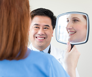 Person looking in hand mirror with health care provider looking on.