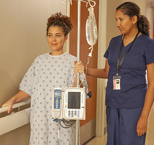 Healthcare provider walking with woman in hospital hallway.