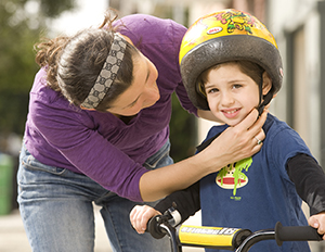 Woman putting helmet on preschooler boy on bike.