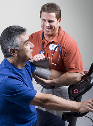 Man exercising on exercise bike while physical therapist takes his blood pressure.