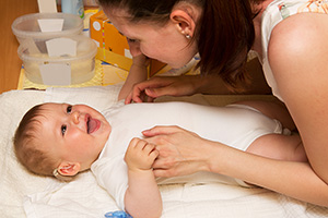 Baby boy with hearing aid in ear laughing and interacting with mother.