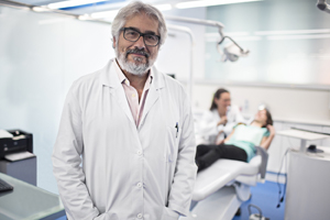 Male dentist standing and smiling in front of an exam chair