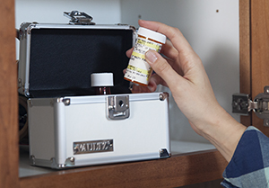 Woman putting pill bottle in locking box in kitchen cabinet.